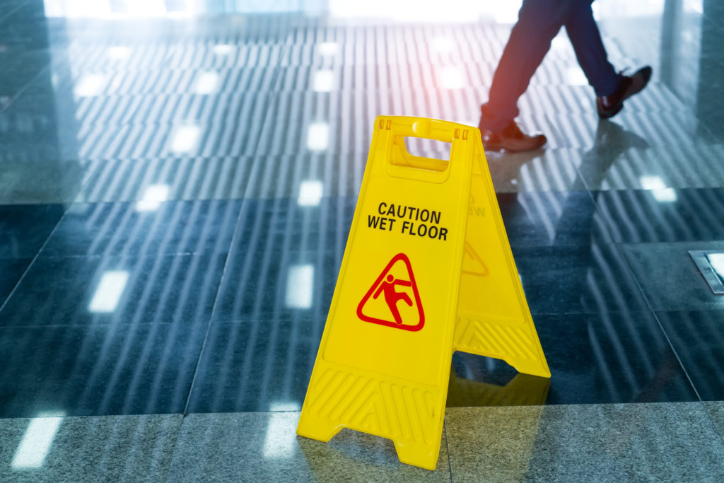 a yellow wet floor sign over a very slippery corridor as a person walks to the right of the frame
