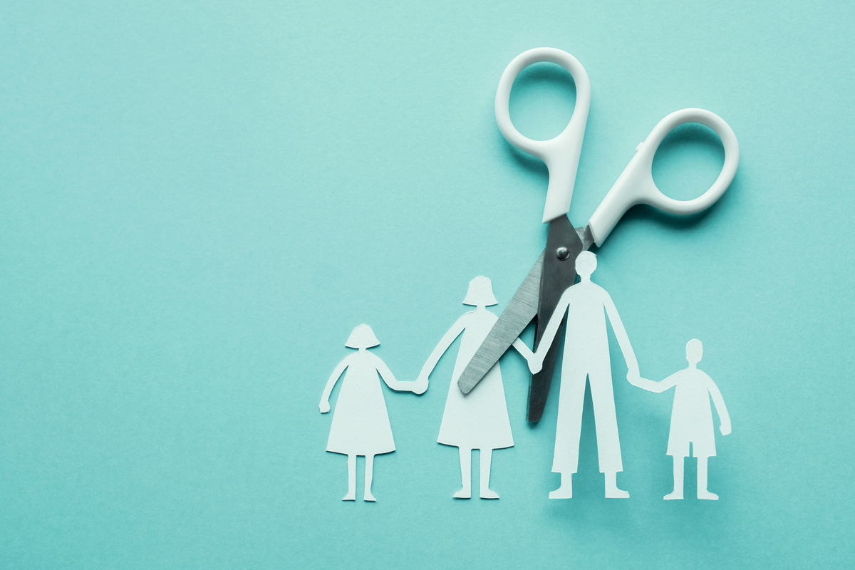 A paper cutout of a family holding hands with a pair of scissors cutting apart the parents.