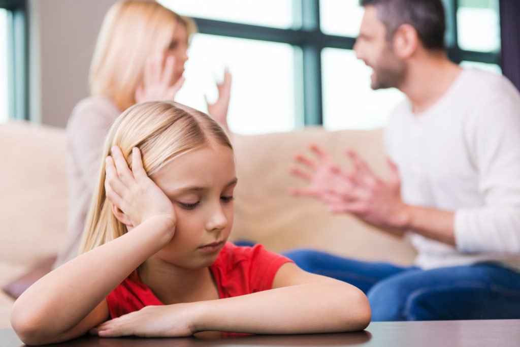 Little girl looking sad as her parents argue in the background