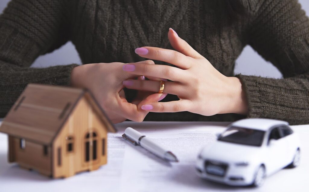 A woman removing her wedding ring near a small model of a home and a miniature car