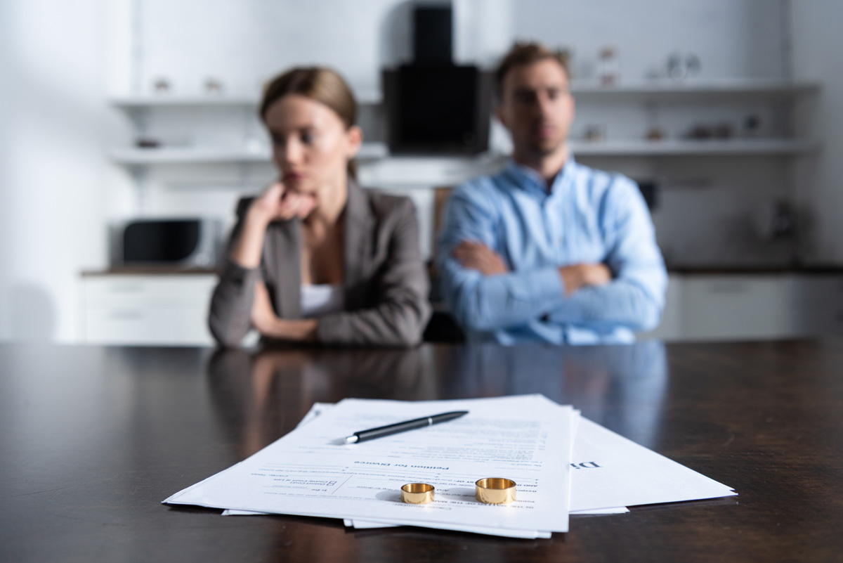 Two people sitting at a table with divorce documents and wedding rings in front of them.