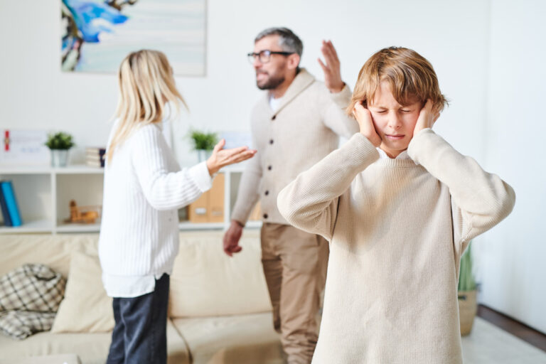 A child covering his ears while his parents have a verbal argument behind him.