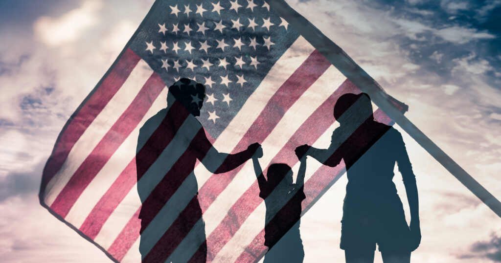 The silhouette of a family holding hands in front of an American flag.