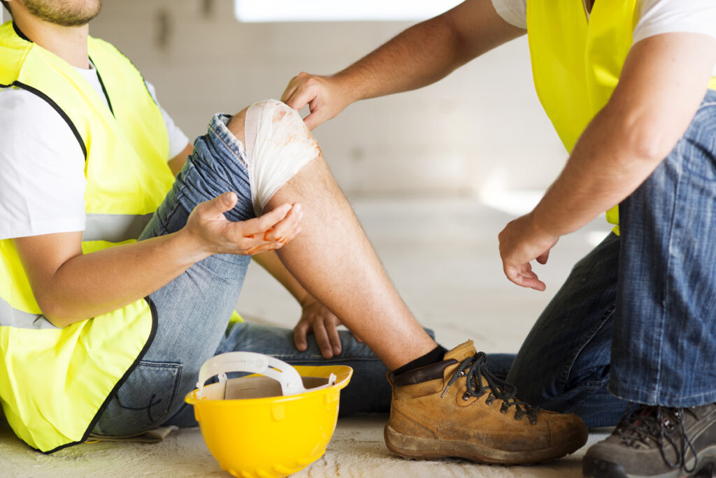 A person with a yellow vest sitting on the ground with another person bandaging their knee in El Paso.